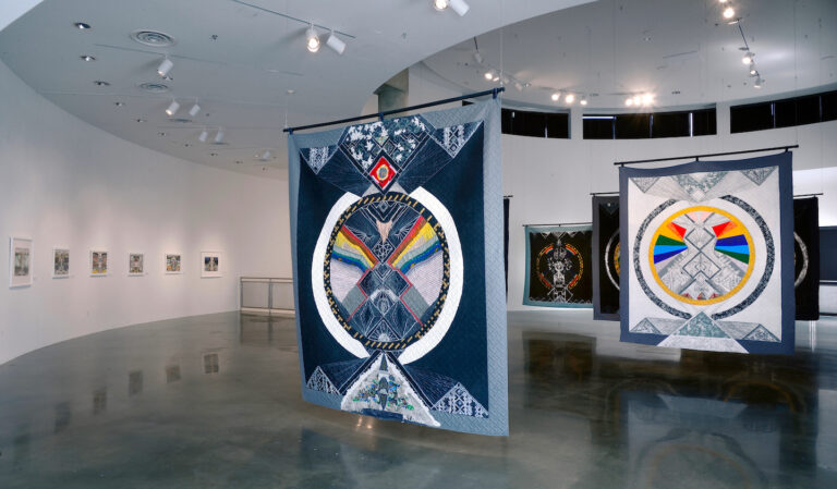 Large two-sided decorative quilts hang from the gallery ceiling.