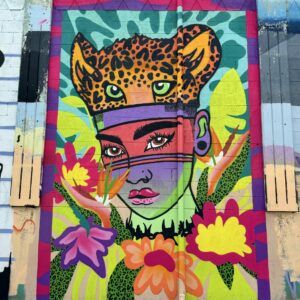 A colorful mural of a Taino person surrounded by tropical flowers wearing a leopard face as a hat.