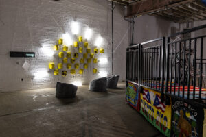 Yellow paper-mâché masks hung up on a wall surrounded by 9 bright lights.