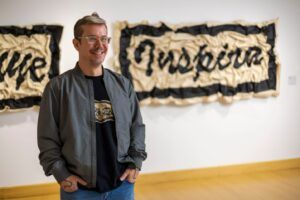 Quintín Rivera Toro stands in a gallery in front of his work.