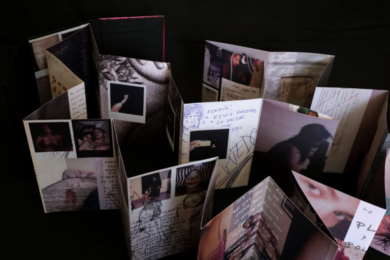 An accordion-style photo book containing journal pages and drawings spread over a table.