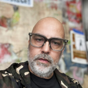 A close up photo of artist Paul Thulin-Jimenez. He wears glasses and looks at the camera with a neutral expression.