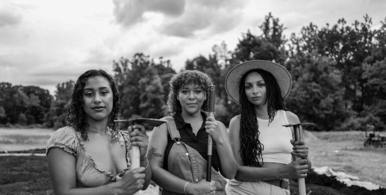 Black and white photo of three women of color standing with their farming tools.