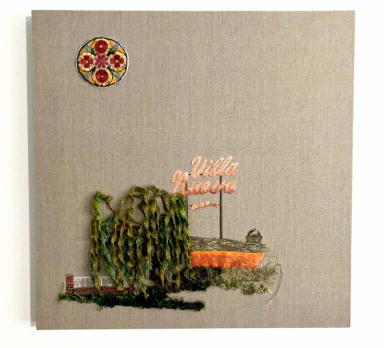 An embroidered tree and fence next to an embroidered sign that reads "Villa Nueva," all on grey linen. In the top left corner there is an embroidered stained-glass window.