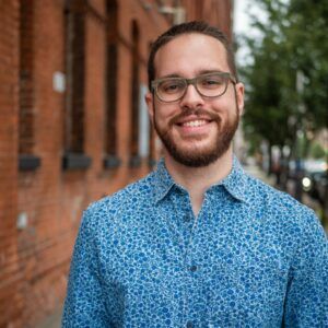 A photo of artist Gabriel Bouche Caro. He wears glasses and smiles at the camera.