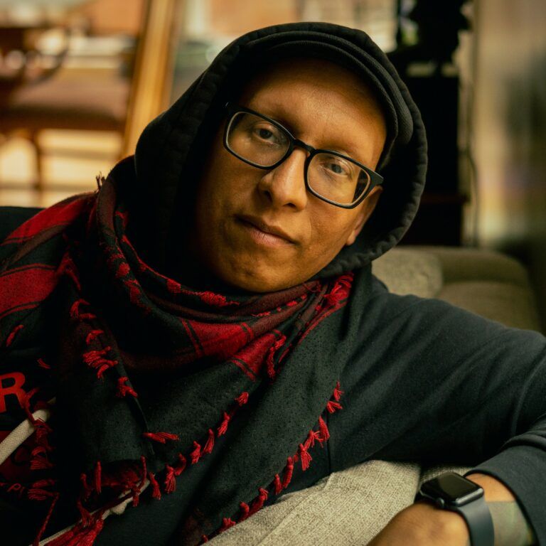 Lantz Arroyo reclines on a couch, smiles slightly at the camera.