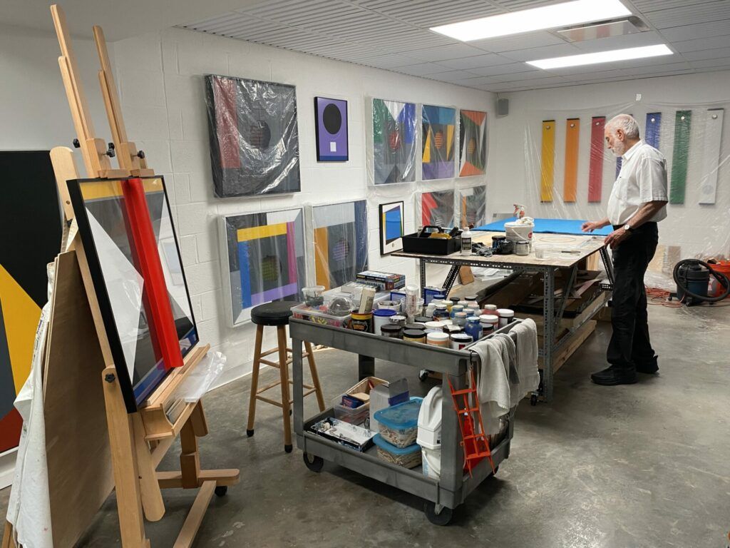 Lope Max Díaz in his studio. He is at a workbench with paints and supplies.