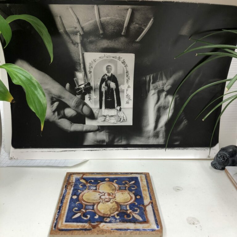 An image of a photograph where a person holds a saint card. There is a colorful tile in the foreground.