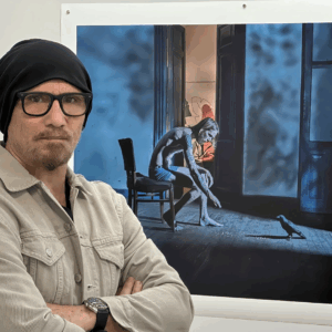 Artist Larry Louie Gonzalez standing in front of a blue and orange painting.