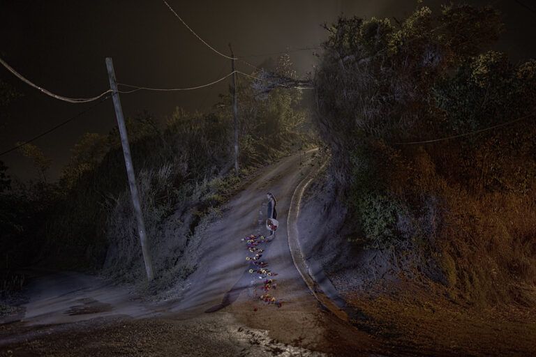 A dark road where a woman stands with flowers scattered by her feet.