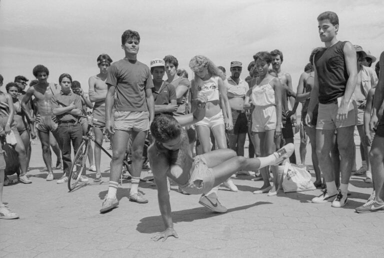 A man breaks dance as a crowd watches on the boardwalk in Orchard Beach in the Bronx in the summer of 1984.