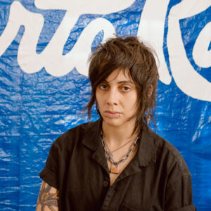 Portrait of Jo Cosme in front of a blue tarp that reads 