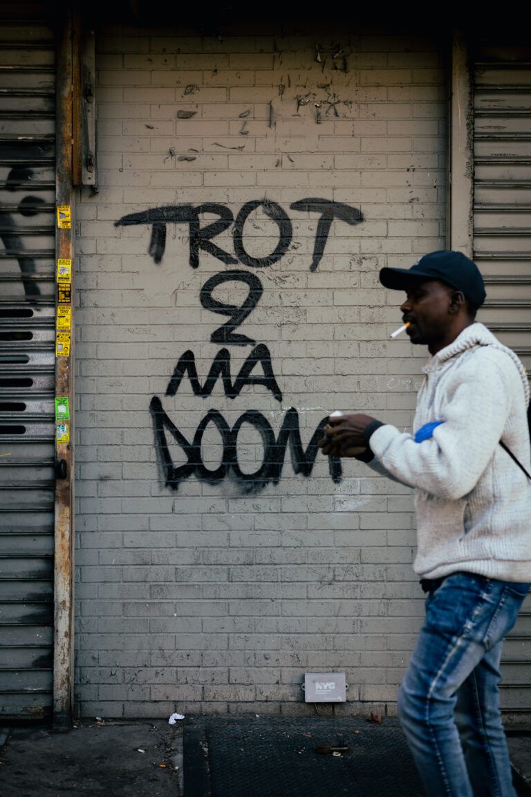 A man smoking walks past graffiti that reads "Trot 2 Ma Doom."