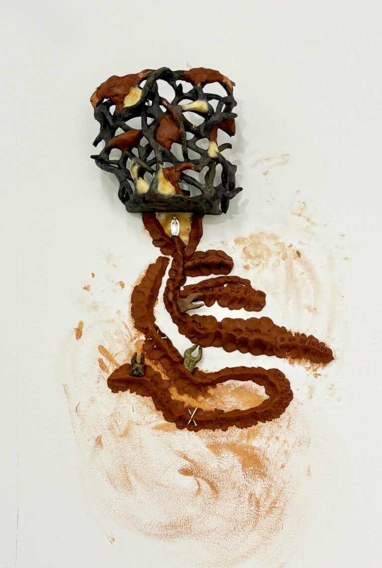 Abstracted sculptural form featuring a lattice of fired clay and small objects set in wet red clay.