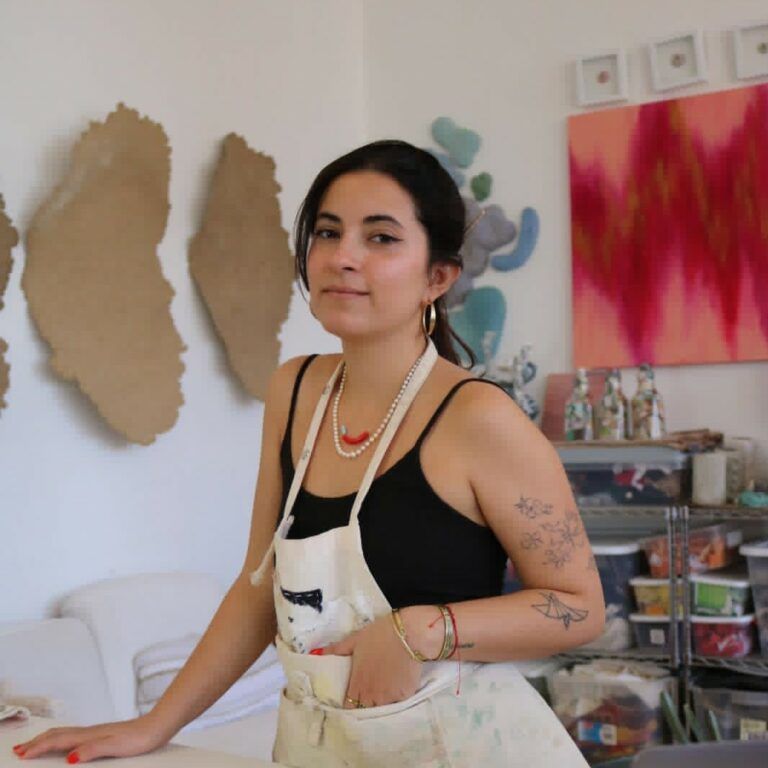 Artist Carla González Asencio in her studio wearing an apron over dark clothes.