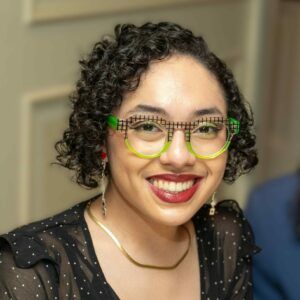 Tracey Reveron smiles at the camera. She wears green glasses.